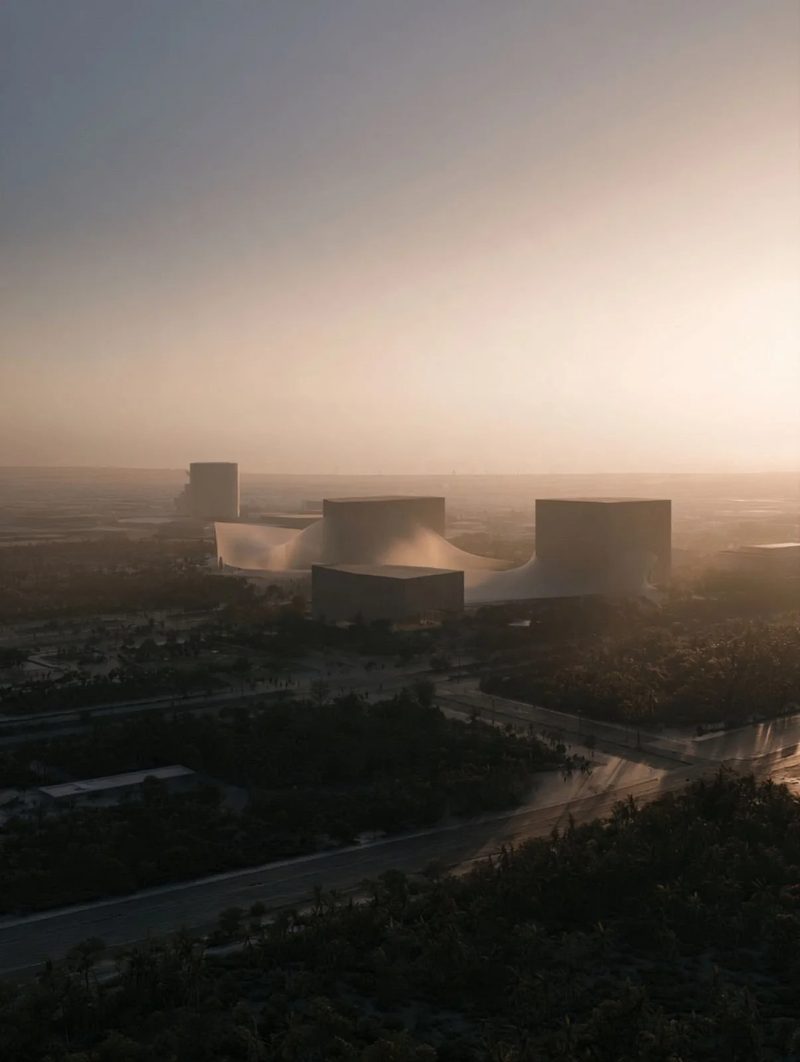 M3 · Árdh, concept image — hazy sunrise over the green edge of a city, low buildings with curved roofs in the distance